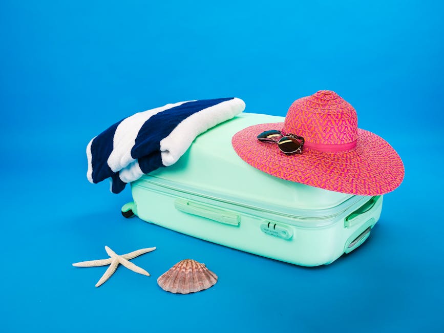 Beach essentials including a suitcase, hat, towel, and seashells on a bright background.
