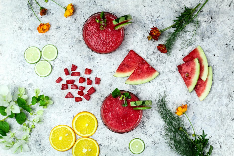 Flat lay of watermelon, citrus slices, herbs, and juice on a textured surface.